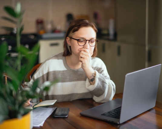 Young woman with laptop reviewing banking or financial papers/statements at home