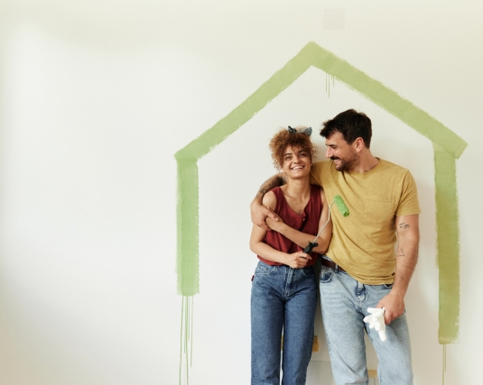 Happy couple standing embraced in the lines of house shape made of green paint on the wall during renovation of their new home