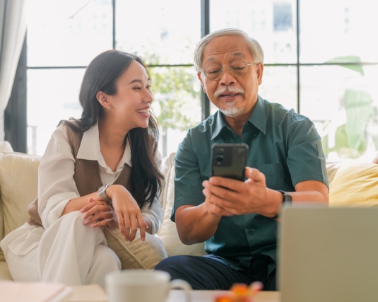 Older father and young daughter happily looking at a cell phone.