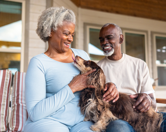 A smiling happy older retired couple playing with their dog