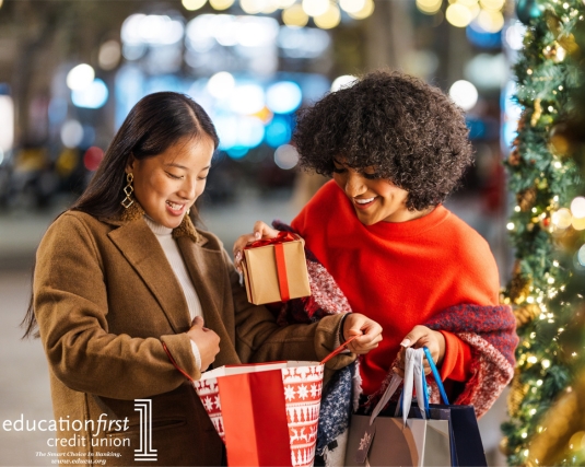 Two smiling young women exchanging gifts in a decorated city street