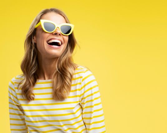 yellow background, happy excited young woman wearing glasses