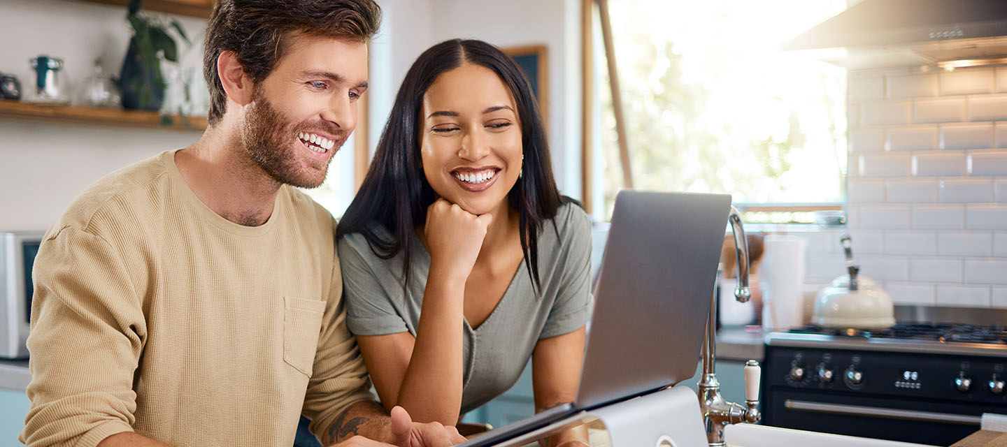 Smiling couple looking at a laptop in the kitchen