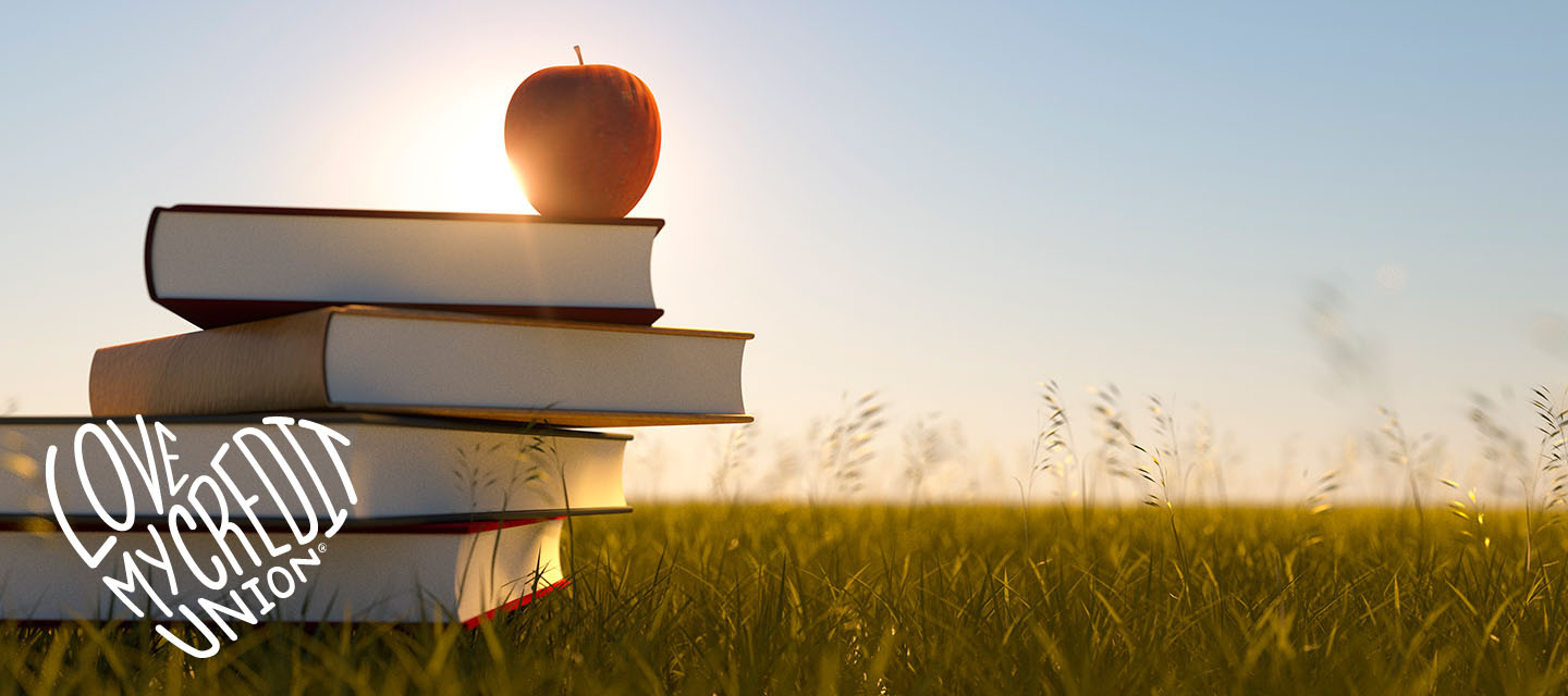 Stacked books with an apple on top in a field