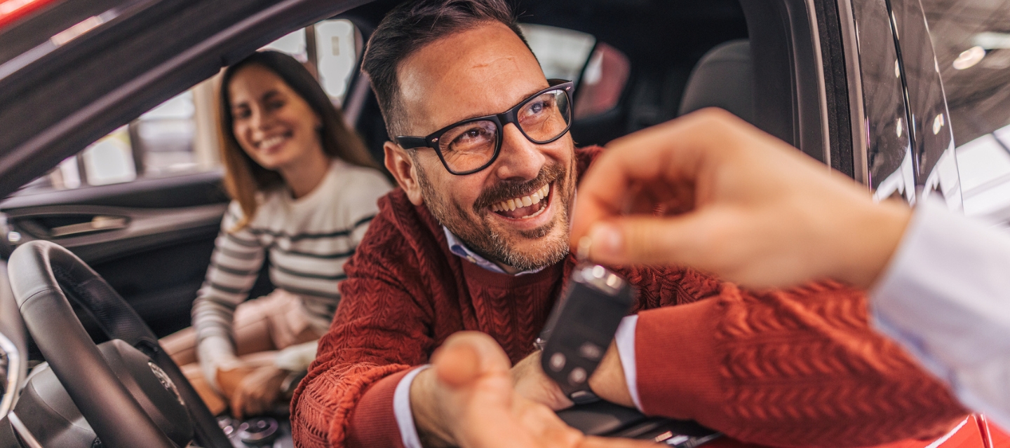 A couple sitting in a car, receiving the keys from a car dealer stock photo.