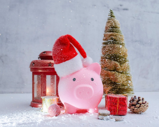 Pink piggy bank wearing Santa hat with Christmas tree, red lantern, gift boxes and snow.