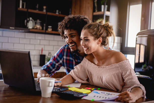 Couple at kitchen table looking at a laptop computer