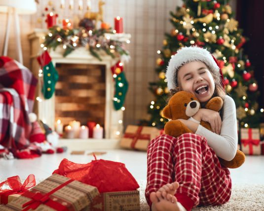 A young girl holding a teddy bear received as a holiday gift