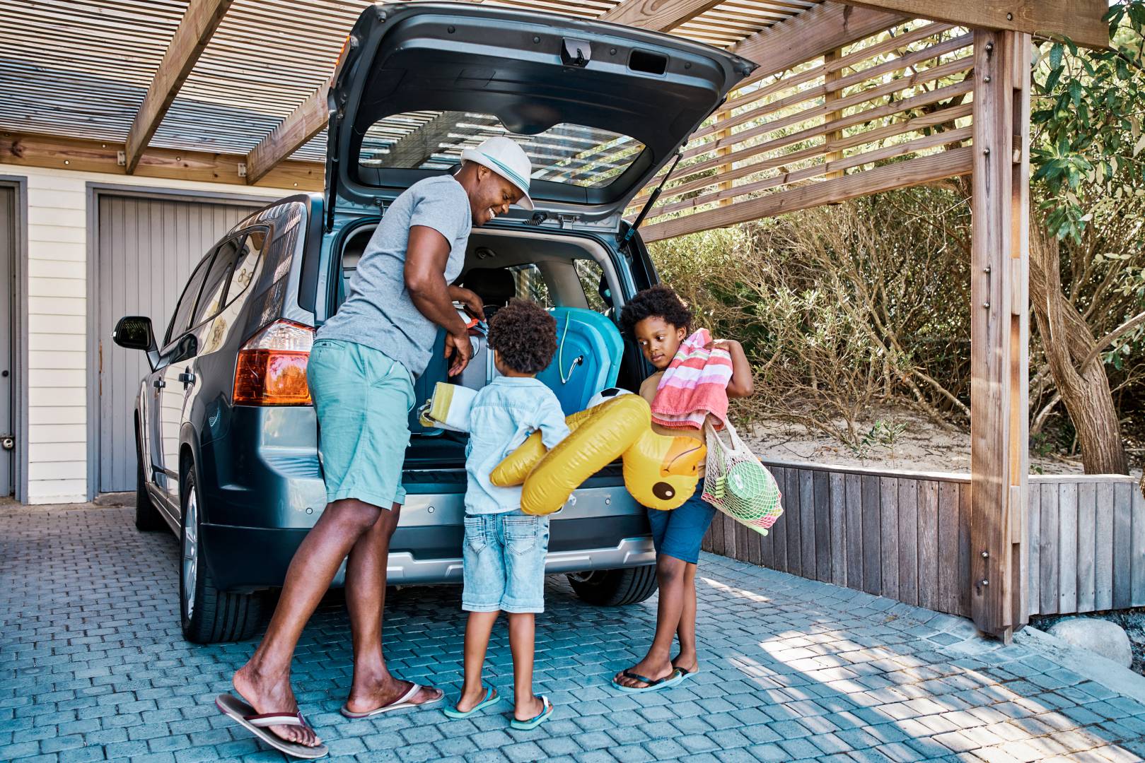A family packing the car to leave for summer vacation. A happy African American father and his two cute little sons preparing the luggage in his vehicle to go on a road trip
