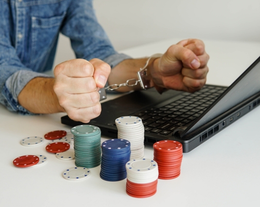 Young addicted man with handcuffs playing online casino poker on laptop.