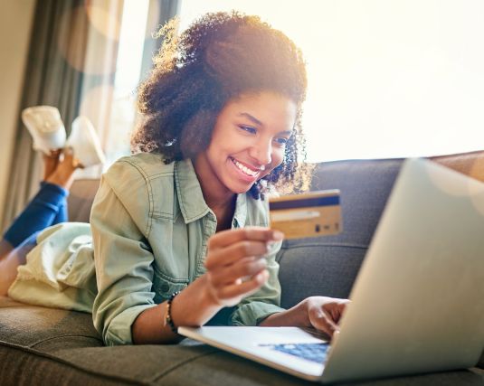 Young woman shopping online at home, using a credit card at home.