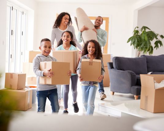 Smiling Family Carrying Boxes Into New Home On Moving Day